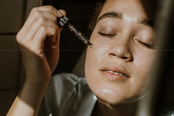 Young woman applying serum on cheekbone of face. 