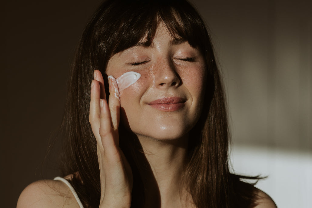 Women applying paraben-free face cream to the check of her face with the sun radiating on face